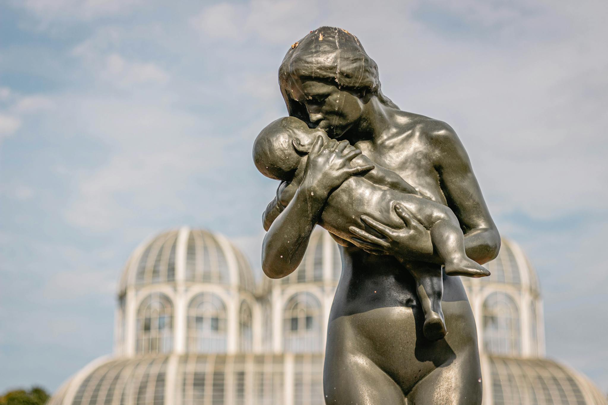 Bronze mother and child statue at Curitiba's Botanical Garden under blue skies.